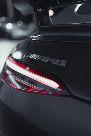 Close-up of a Mercedes AMG logo on a glossy black car with blurred city lights in background.