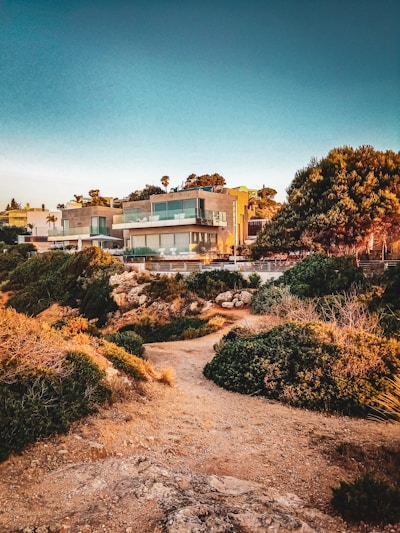 Elegant modern villa with large glass windows overlooking a serene garden at sunset.