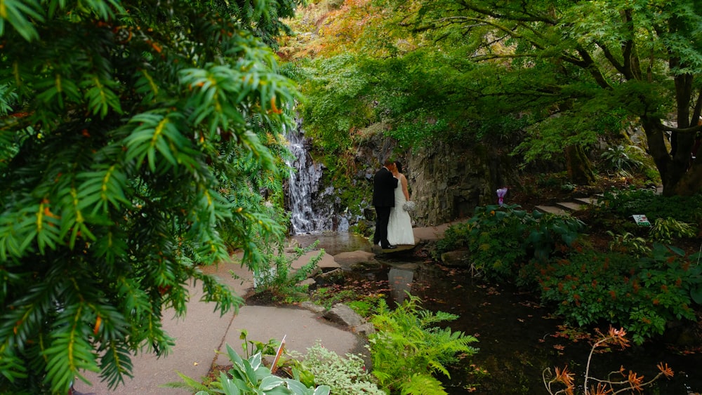 a bride and groom standing in front of a waterfall