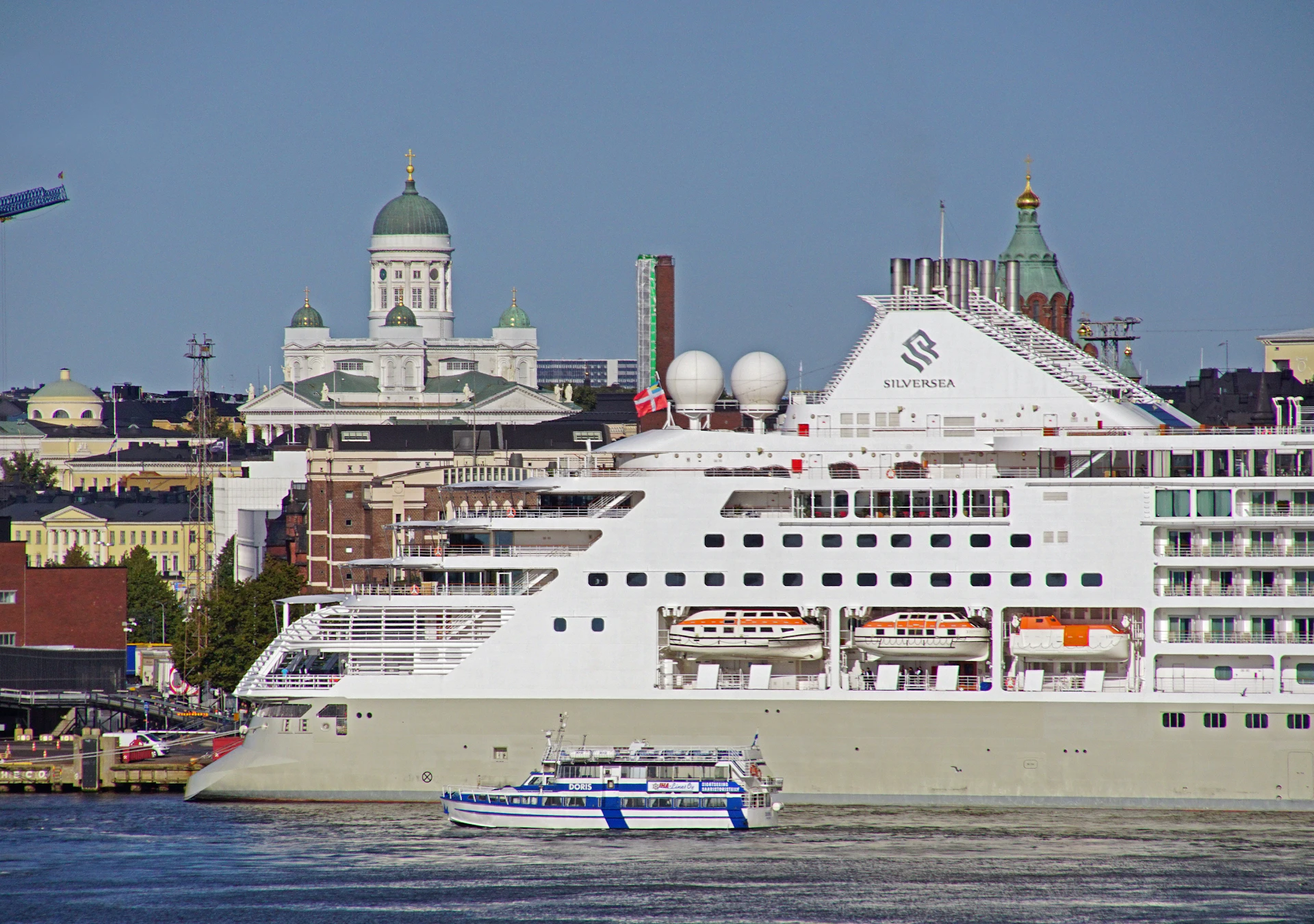 A panoramic view of a majestic cruise ship docked near a bustling European port city with historic architecture.