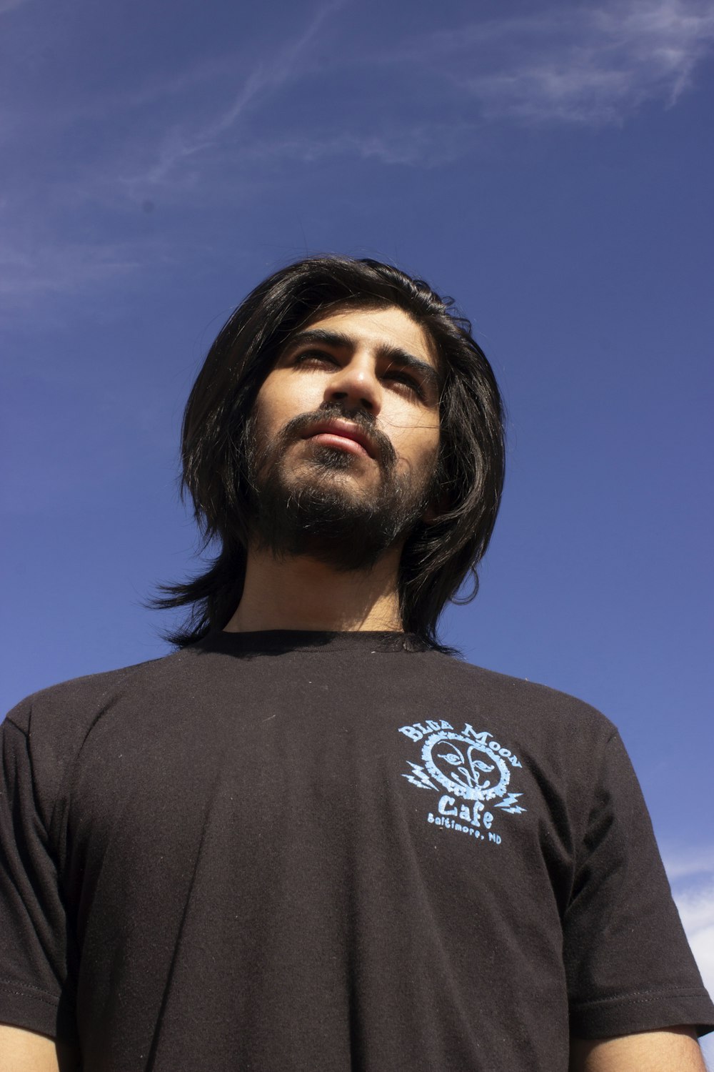 um homem de cabelos compridos e barba em pé diante de um céu azul
