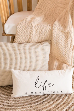 A knitted leisure blanket draped over a comfy chair next to a floral decor pillow.