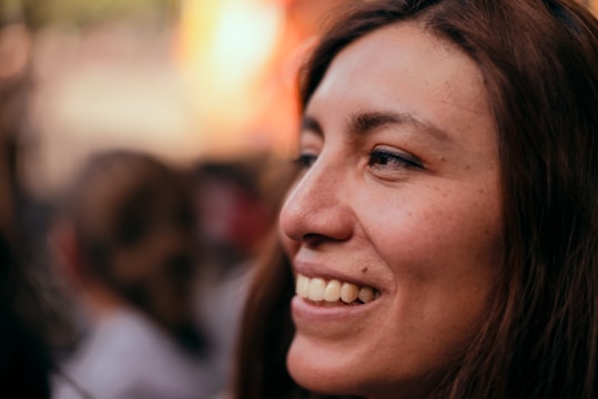 A close-up portrait of a smiling woman with soft natural light and cityscape behind.