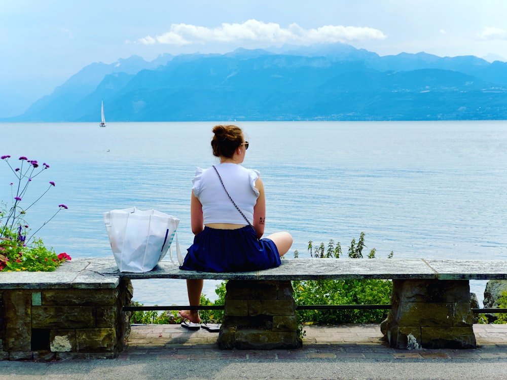 a woman sitting on a bench looking at the water