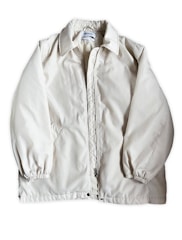 A light beige or off-white jacket with a zipper closure and a collar. The jacket has long sleeves with elastic cuffs and side pockets. The fabric appears to be smooth and slightly shiny. A label is visible on the inside near the collar.