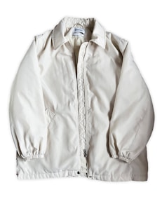 A light beige or off-white jacket with a zipper closure and a collar. The jacket has long sleeves with elastic cuffs and side pockets. The fabric appears to be smooth and slightly shiny. A label is visible on the inside near the collar.