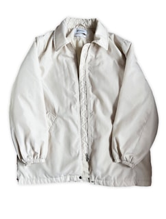 A light beige or off-white jacket with a zipper closure and a collar. The jacket has long sleeves with elastic cuffs and side pockets. The fabric appears to be smooth and slightly shiny. A label is visible on the inside near the collar.
