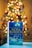 A book titled 'The Christmas Wish' by Nora Roberts is prominently displayed in the foreground, resting on a flat surface. The background features a warmly lit Christmas tree adorned with lights and ornaments, creating a cozy and festive atmosphere.