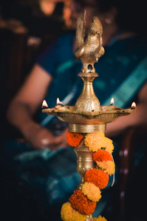 Close-up of Shree Aradhana pooja oil bottle glowing softly beside a lit diya on a brass plate.