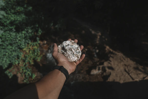 Close-up of a hand holding a weathered staurolite fairy cross rock against a backdrop of Minnesota forest.