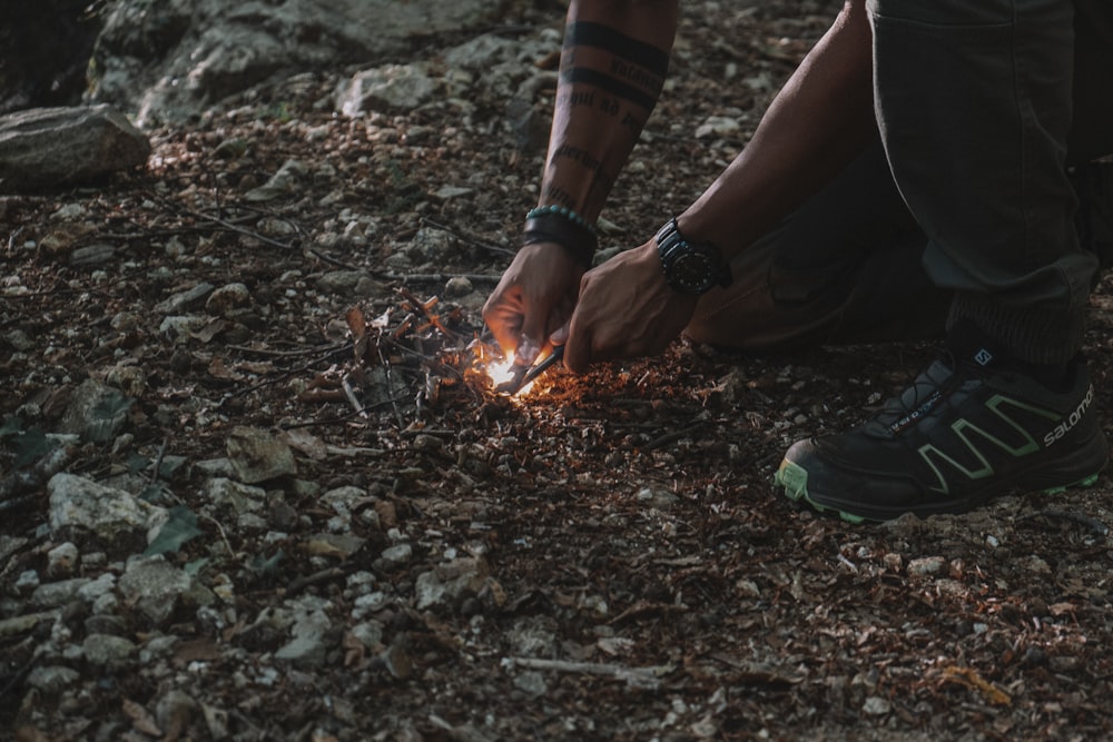 a man kneeling down on the ground with a lit object in his hand