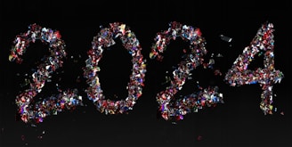 The numbers '2024' are creatively formed using an assortment of colorful, reflective confetti on a dark background. The confetti pieces are predominantly red, blue, and silver, creating a vibrant and festive composition.
