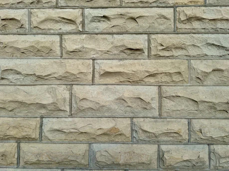 A detailed close-up of hands laying bricks on a rustic stone wall under natural daylight.