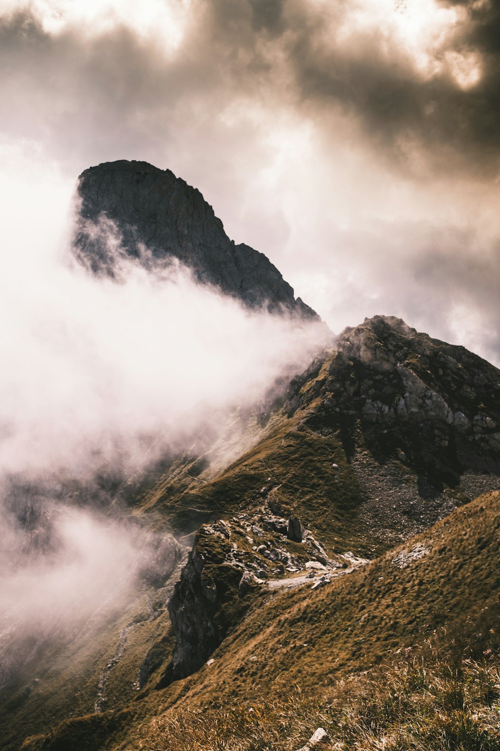 a mountain covered in clouds and grass under a cloudy sky