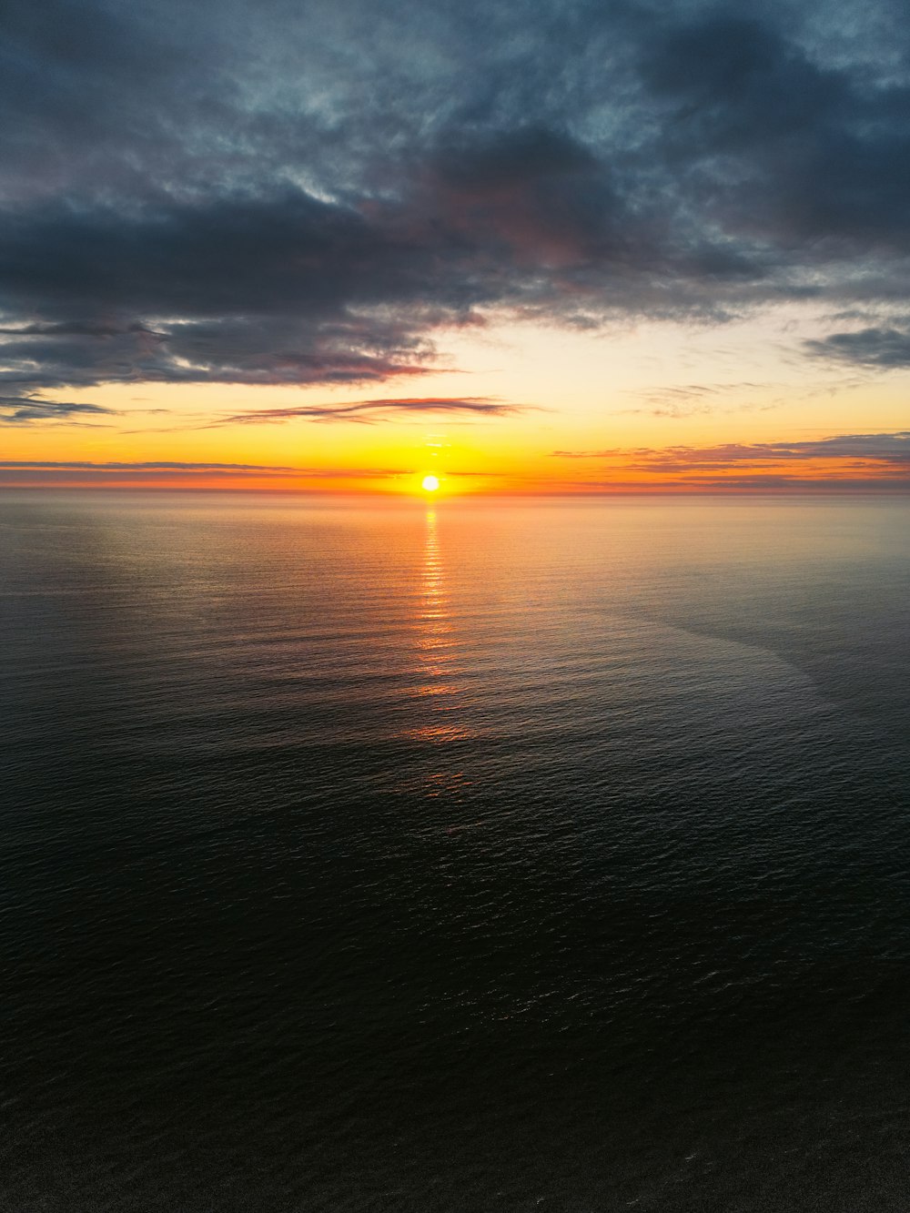 the sun is setting over the ocean on a cloudy day