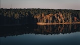 A calm lake reflecting autumn trees in vibrant reds and oranges.