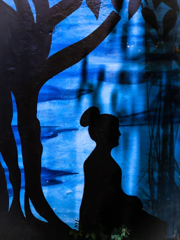 A serene image of a person sitting peacefully under a sprawling tree of life, bathed in soft blue and green light.