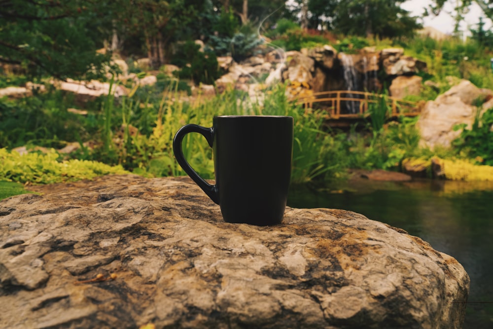 a black coffee cup sitting on top of a rock