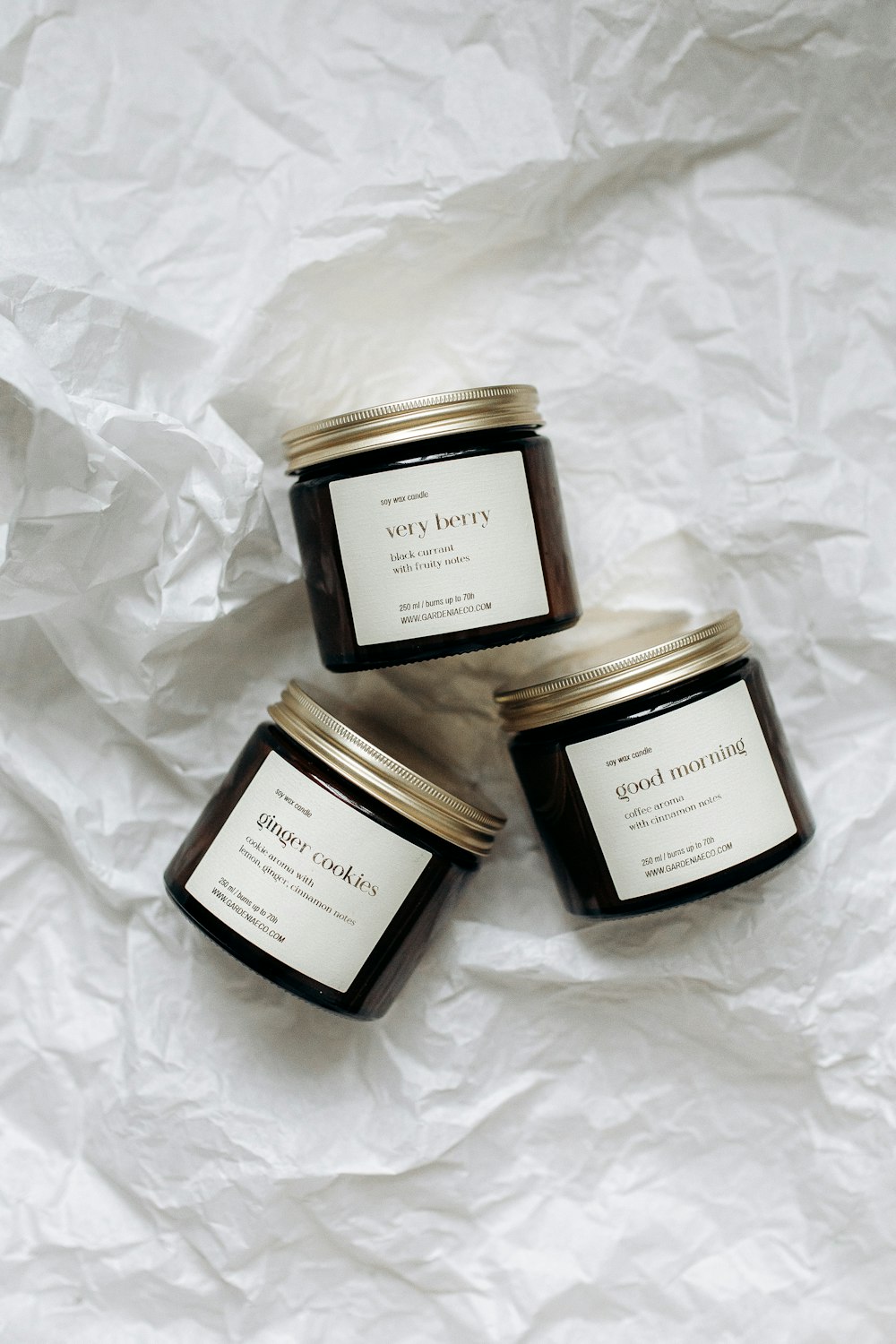 three jars of candles sitting on top of a white sheet