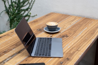 A digital nomad working on a laptop beside a frothy cappuccino, surrounded by plants.