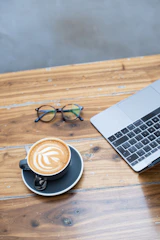 A printed boleto payment slip resting on a wooden table next to a laptop and a cup of coffee.