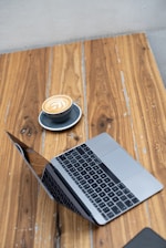 A sleek laptop open on a wooden desk with a cup of coffee nearby
