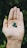 A hand is open with three small, round green pills or beads resting on the palm against a blurred, leafy background.