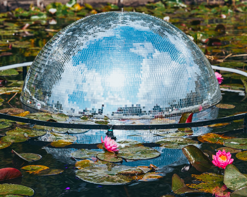 a large mirror ball sitting on top of a pond filled with water lilies