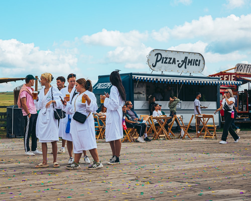 a group of women in white robes standing in front of a food truck