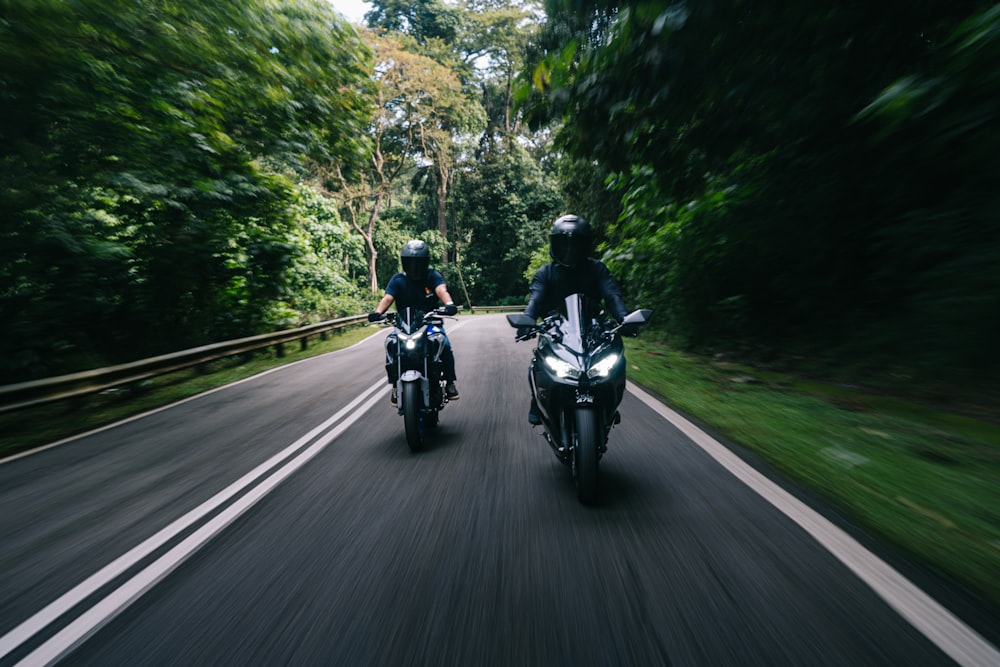 two people riding motorcycles on a road in the woods