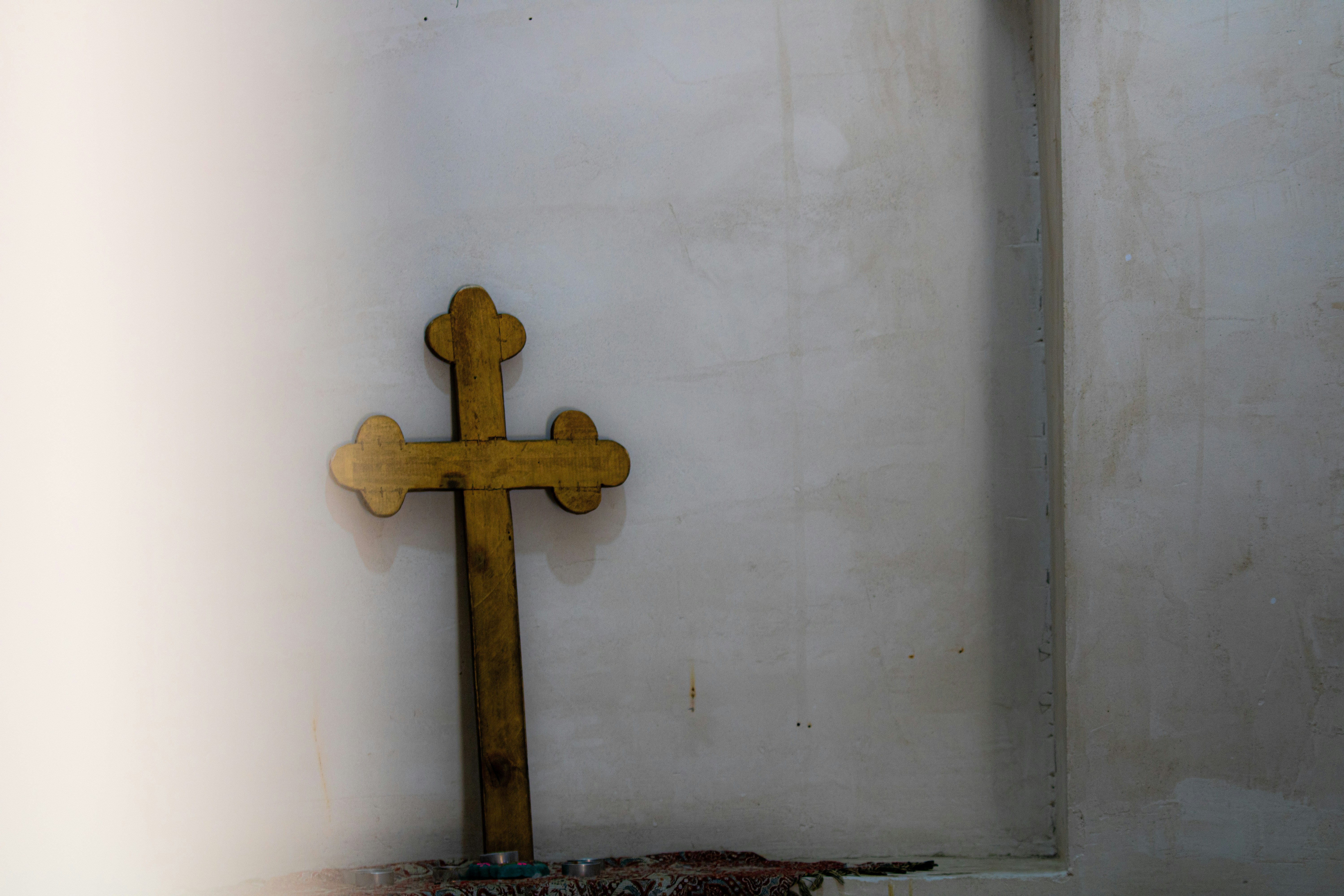 Medium reclaimed oak wood cross with aged natural grain finish mounted on warm white wall, golden hour light
