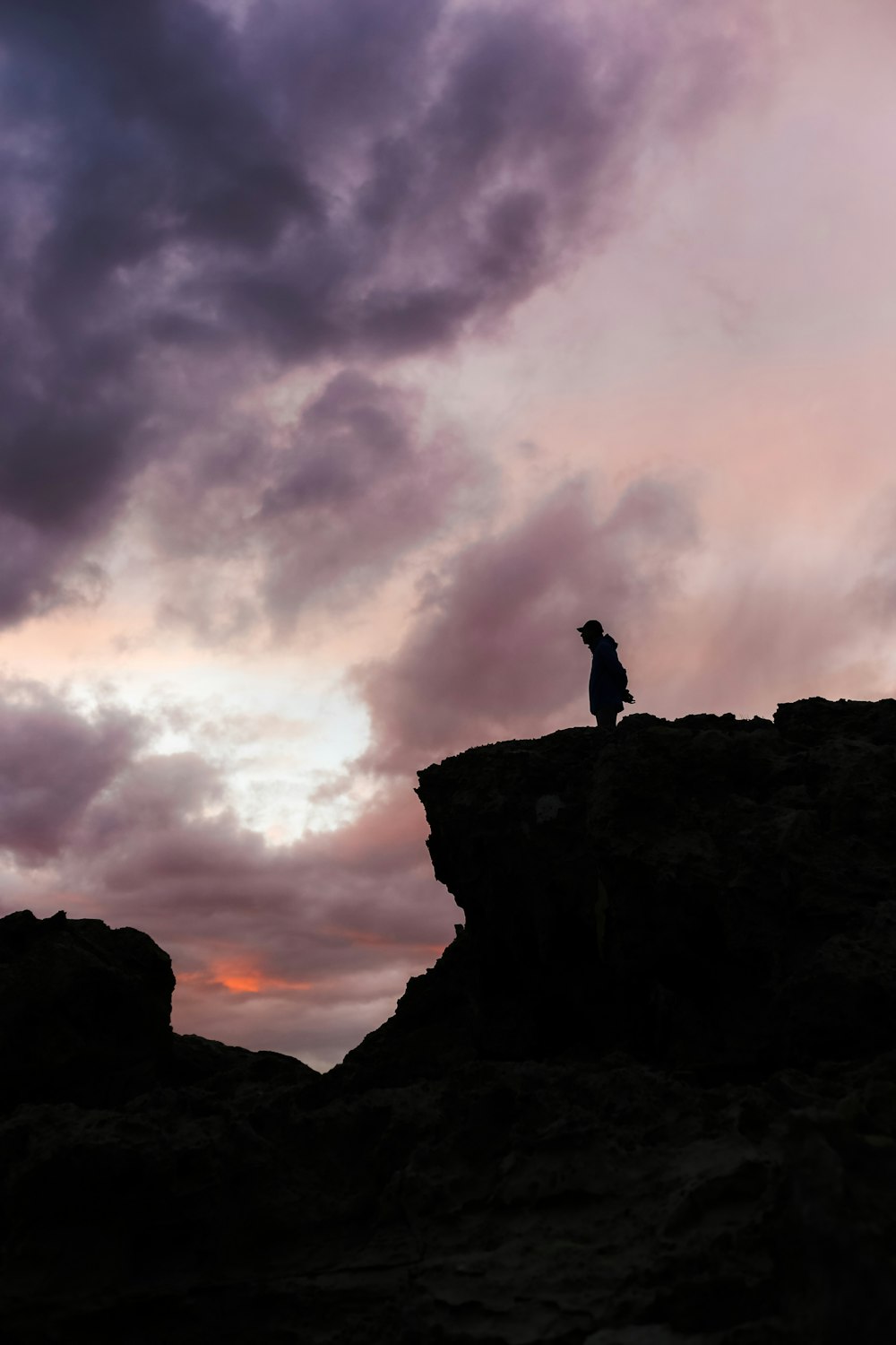 a man standing on top of a rocky cliff under a cloudy sky