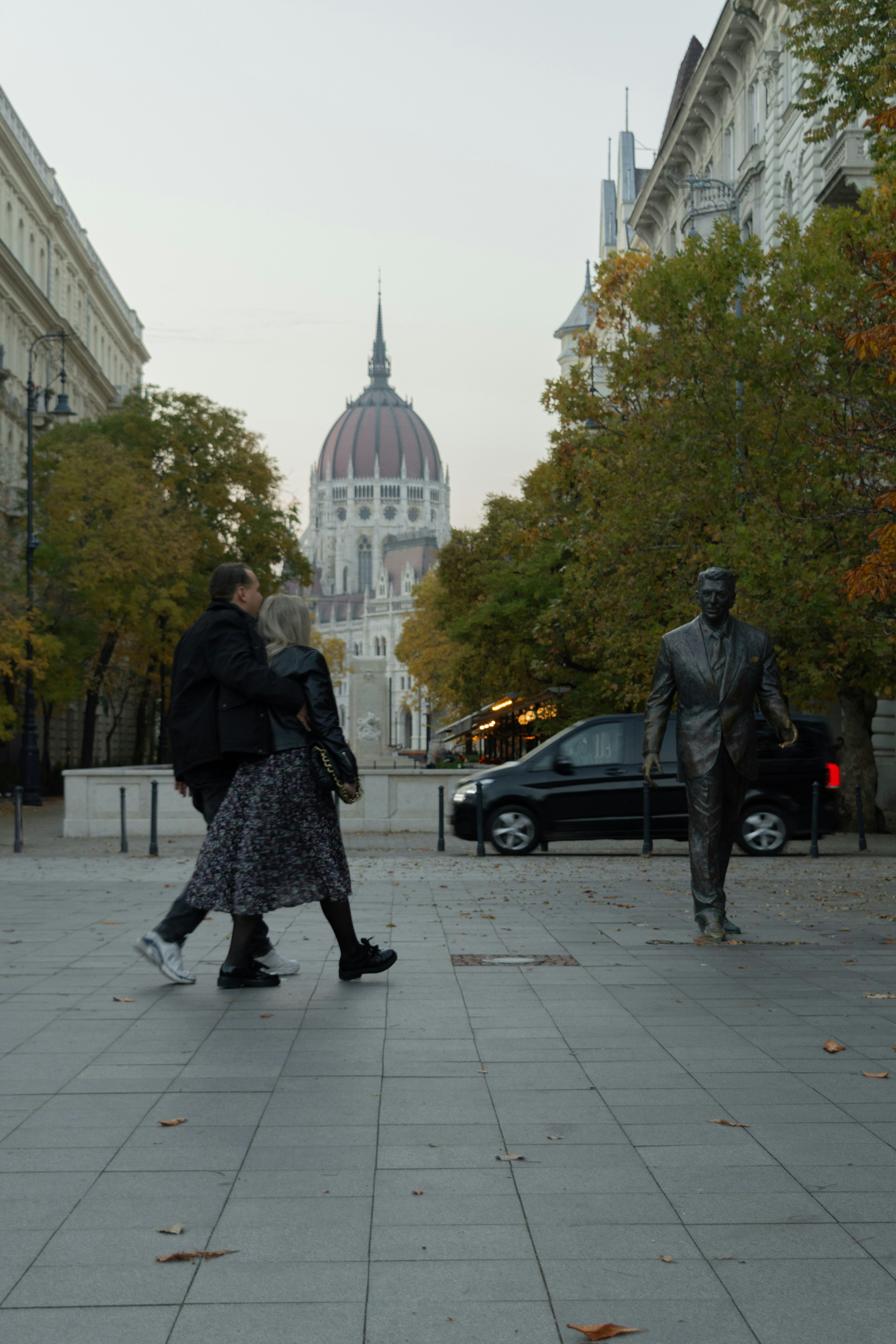 a couple of people walking down a sidewalk next to a statue