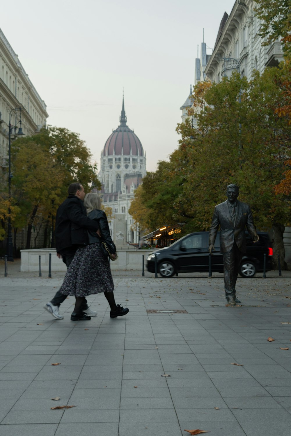 a couple of people walking down a sidewalk next to a statue