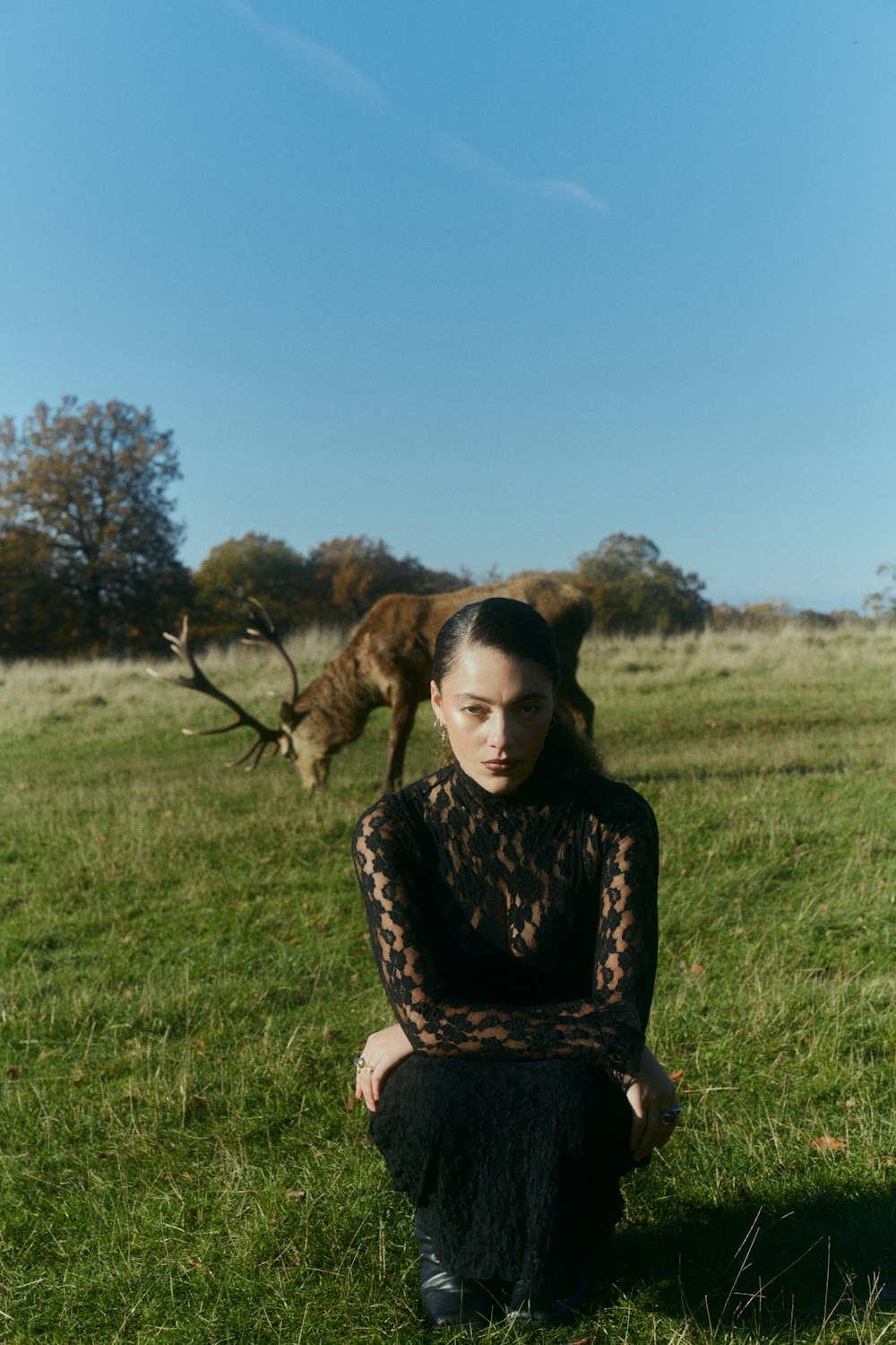 a woman sitting in the grass with a dog behind her