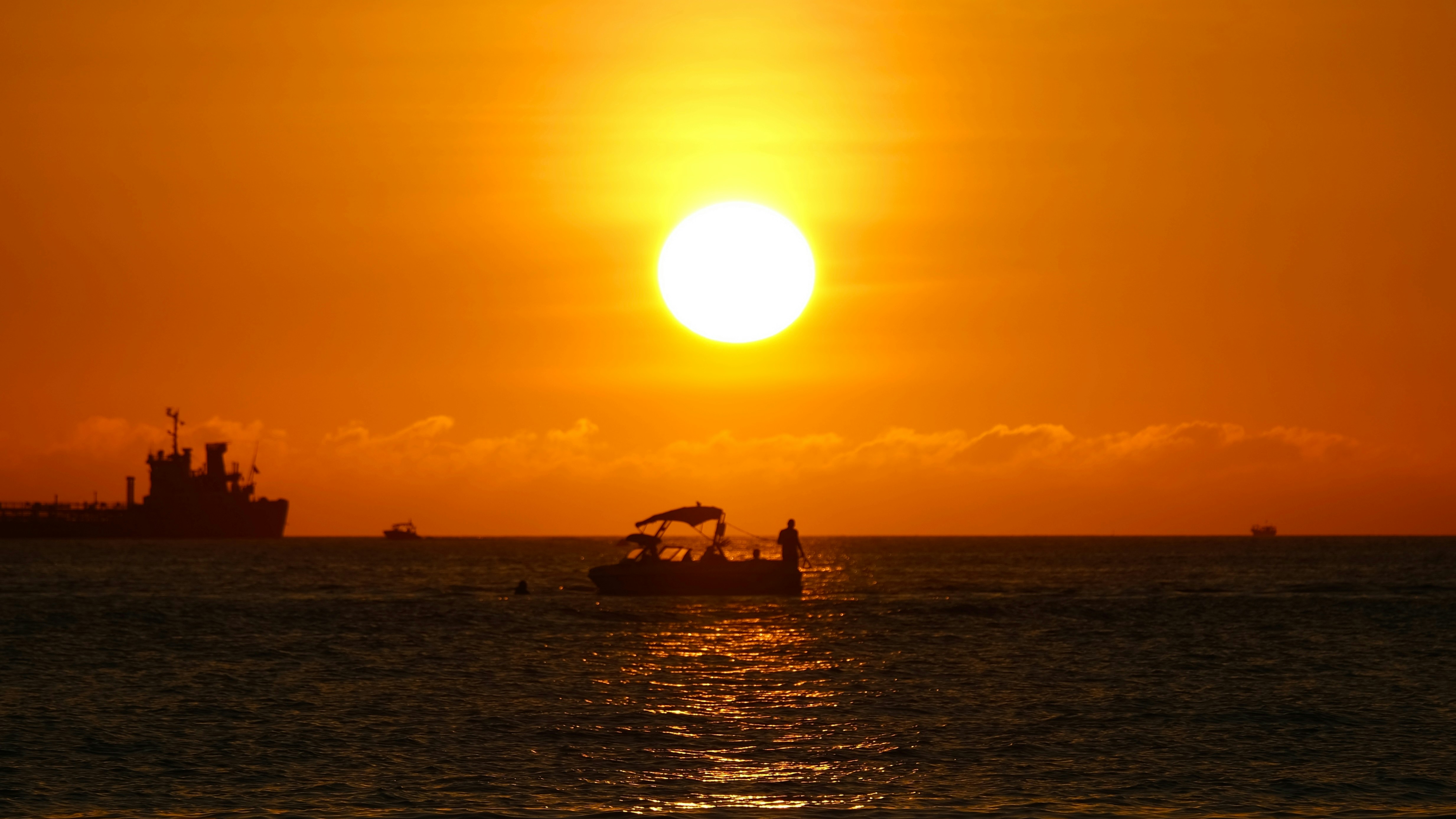 a boat in the water at sunset with a large ship in the background