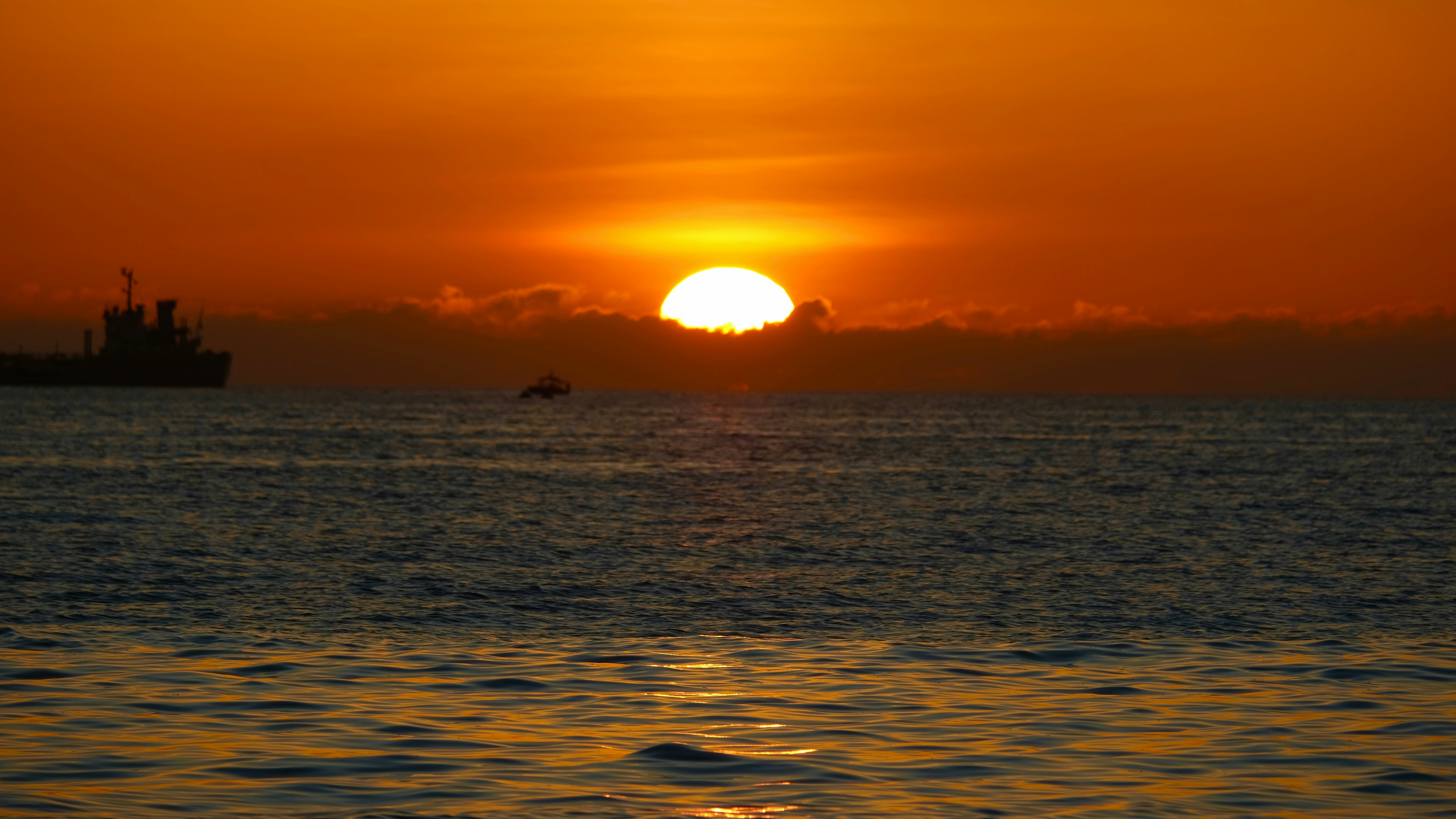 the sun is setting over the ocean with a boat in the distance