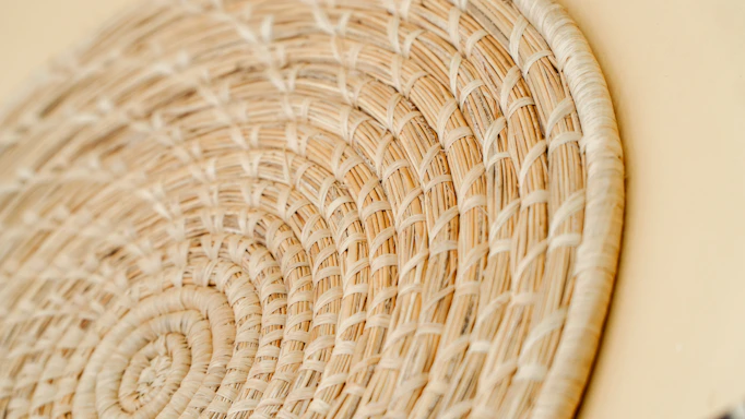 Close-up of artisan's hands weaving a natural fiber basket in soft daylight.