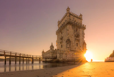the sun is setting behind a tower on the beach