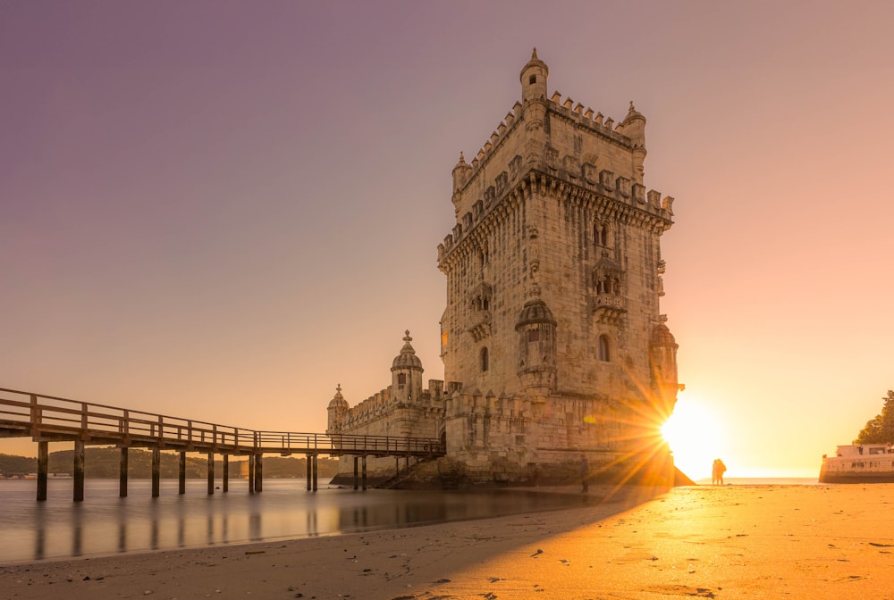 the sun is setting behind a tower on the beach