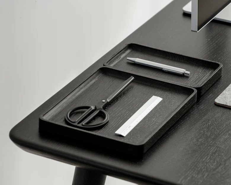 A sleek desk setup featuring a metal pen holder and stackable paper trays neatly arranged on a wooden surface.