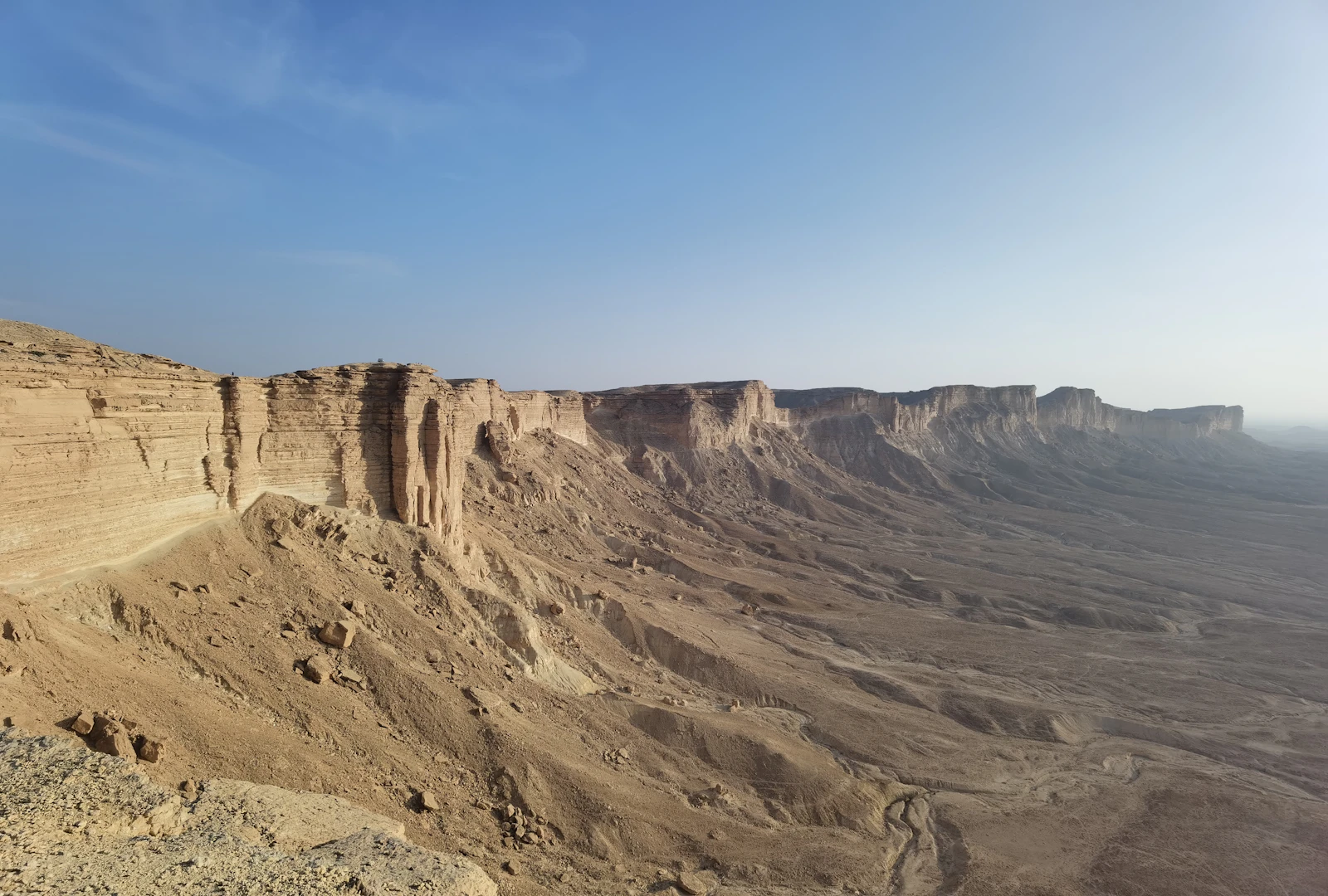 Small figure on dramatic cliff, towering over vast desert landscape in Saudi Arabia