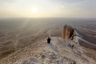 A lone traveler standing on a cliff edge overlooking a vast desert sunset.