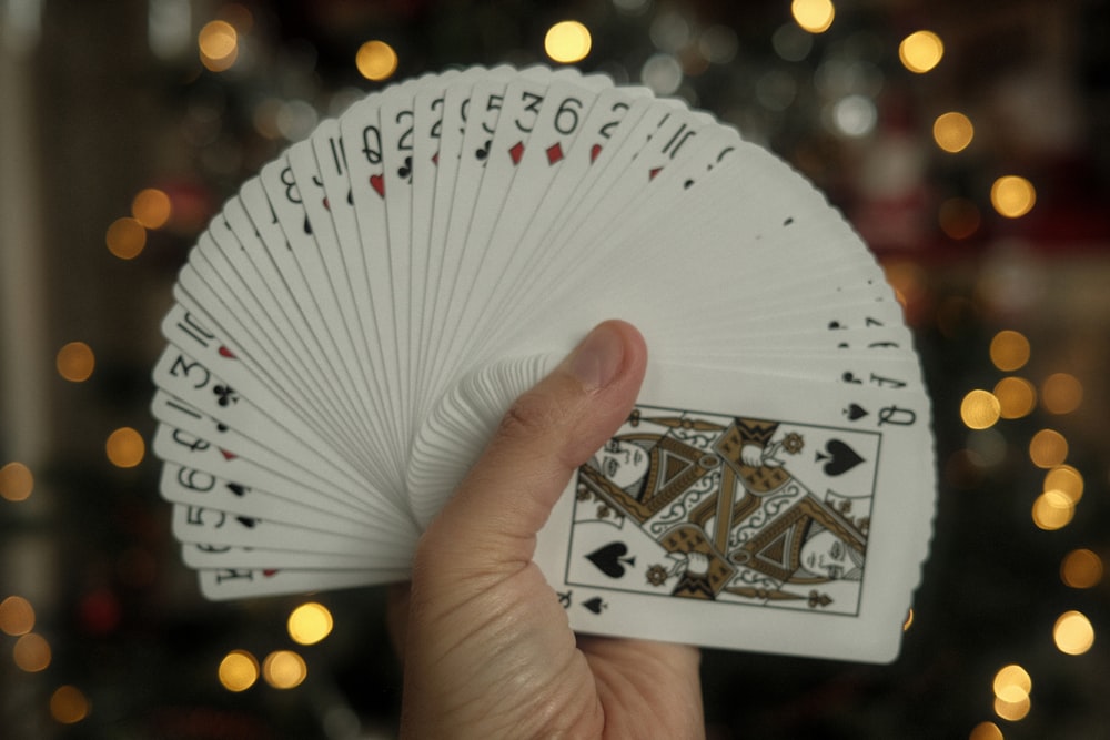 a hand holding a deck of cards in front of a christmas tree