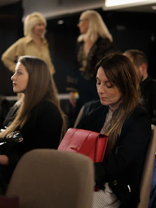A group of smiling women happily exchanging stylish handbags in a cozy, sunlit living room.