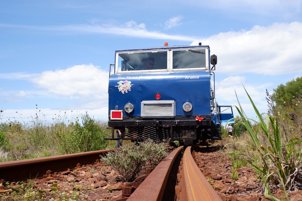 a blue train traveling down train tracks next to a field