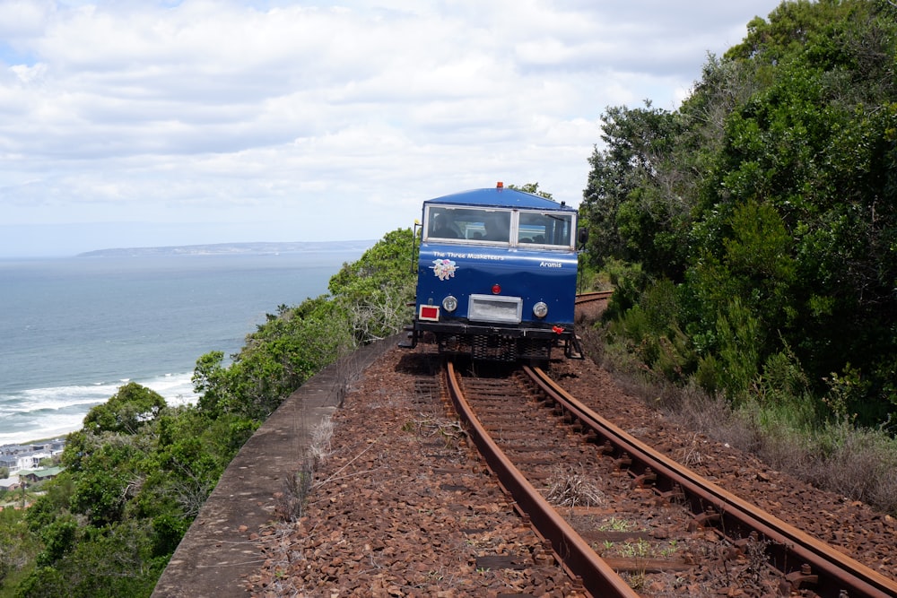 a blue train traveling down train tracks next to the ocean