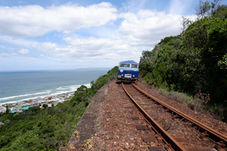 a blue train traveling down train tracks next to the ocean