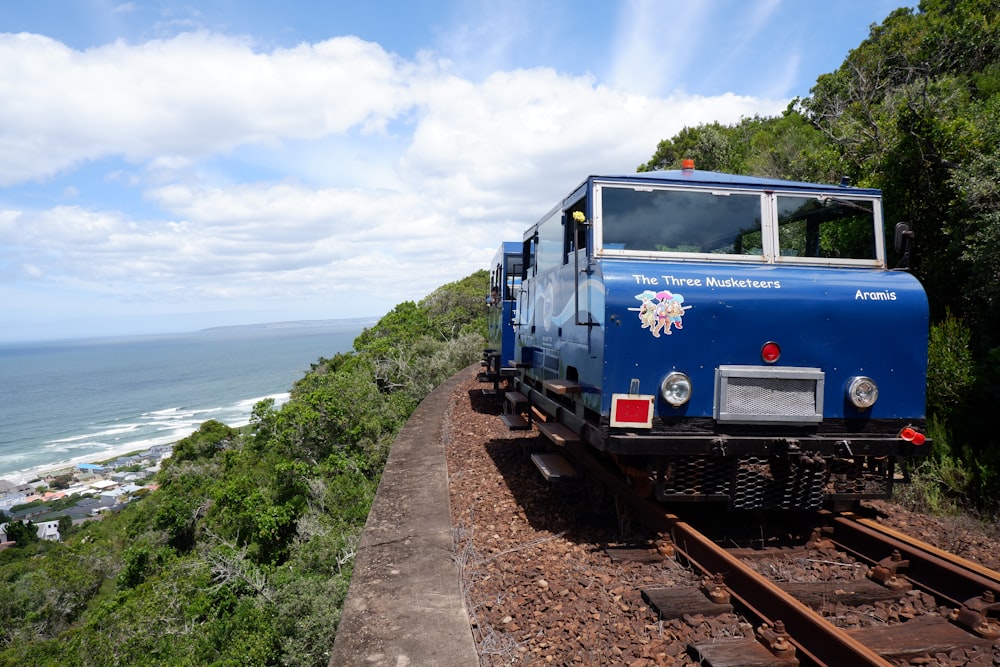 a blue train traveling down train tracks next to the ocean