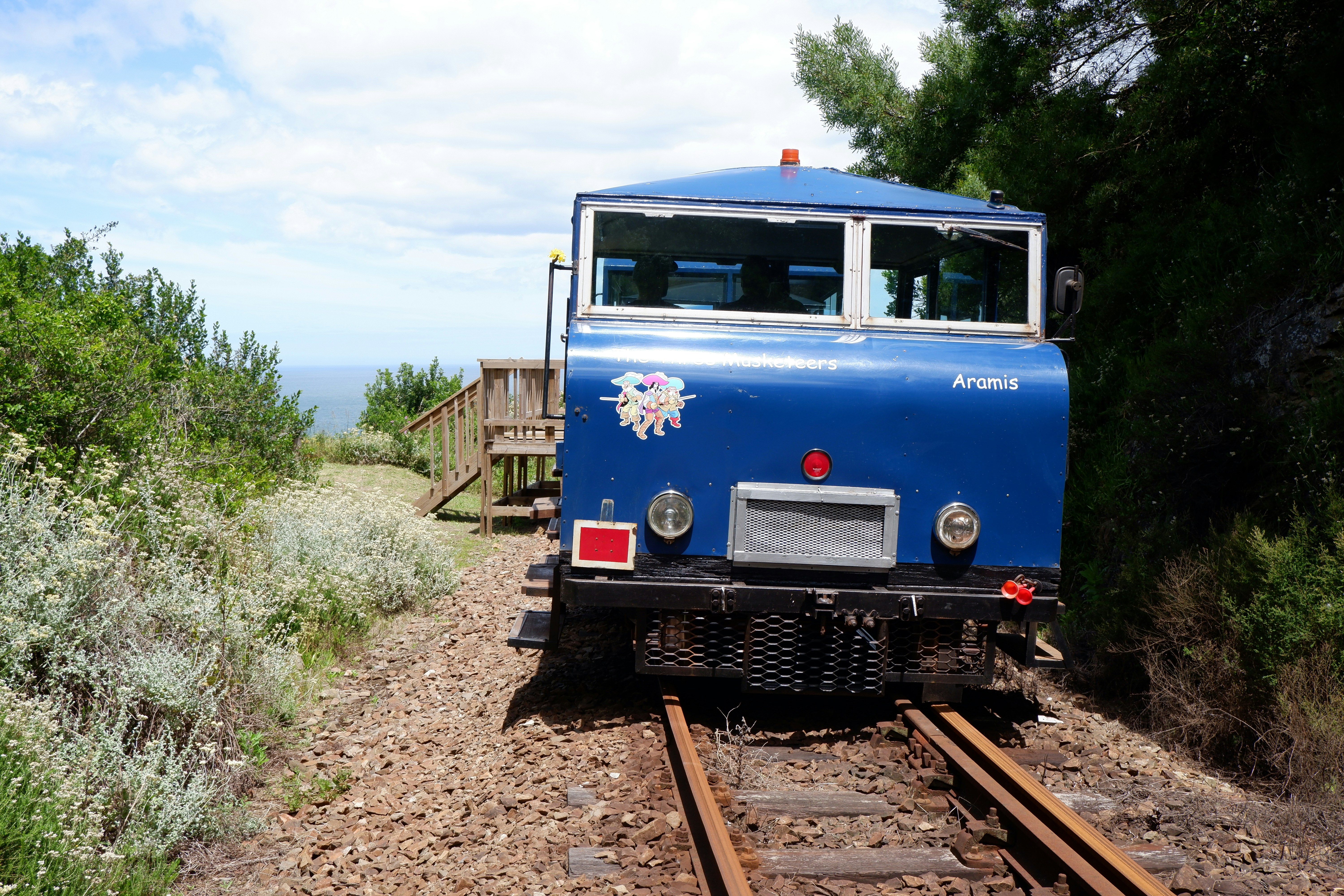 a blue train traveling down train tracks next to a forest
